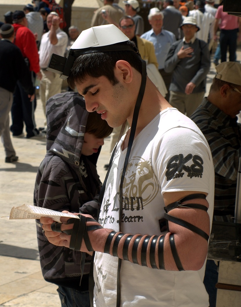 上图:一个犹太年轻人在前额和左臂上佩带经文匣(tefillin),在耶路撒冷